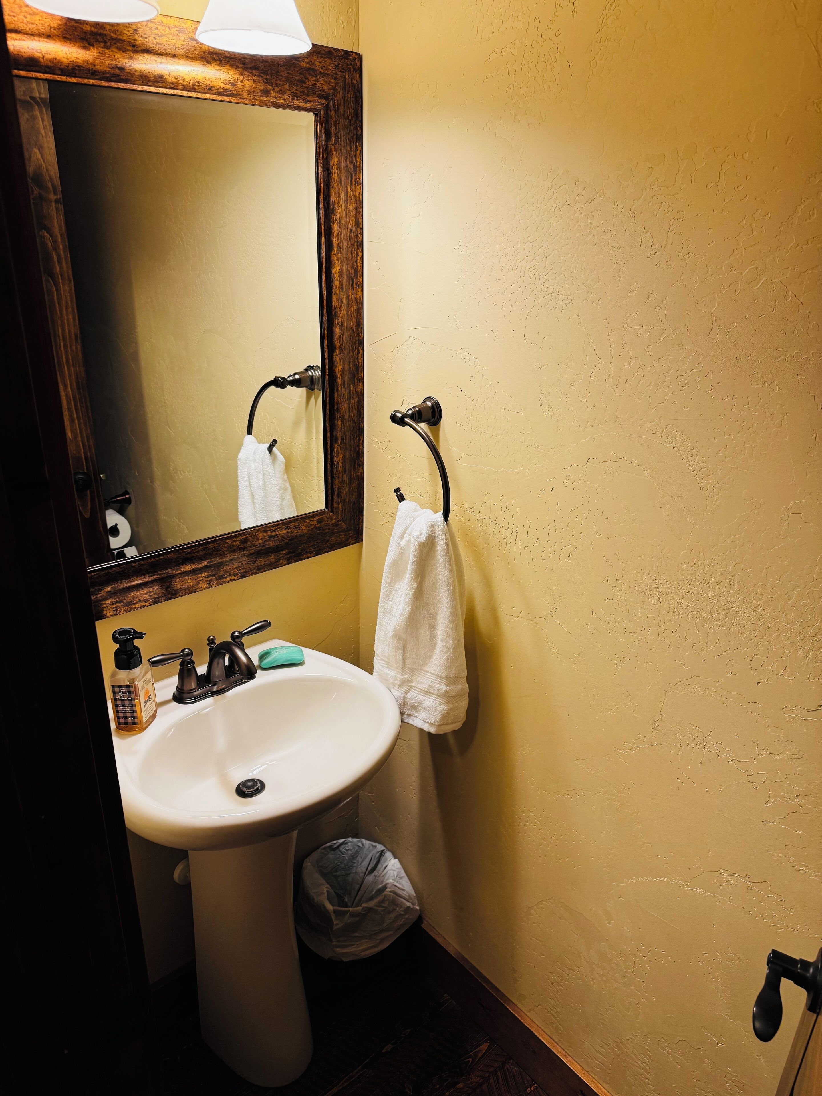 A bathroom with a white sink, a mirror, a towel hanging on a rack, and a trash bin.