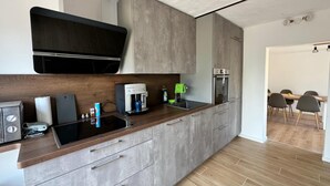 Et moderne køkken med indbygget ovn, kaffemaskine og et spiseområde med bord og stole.