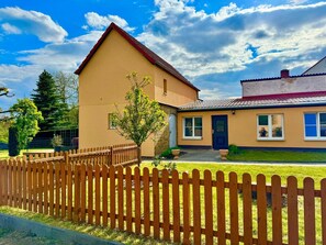 A two-story house with a wooden fence in front, a small tree, and a clear sky.