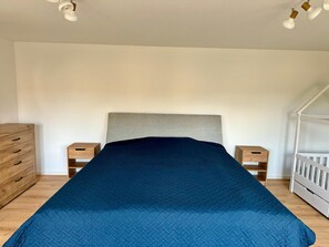 A bedroom with a bed, a wooden dresser, two bedside tables, and a crib. - Ferienhaus Havelzeit in Werder an der Havel (Werder (Havel))