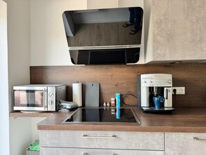 Une cuisine équipée d’un four à micro-ondes encastré, d’une machine à café et d’un téléviseur à écran plat fixé au-dessus du plan de travail.