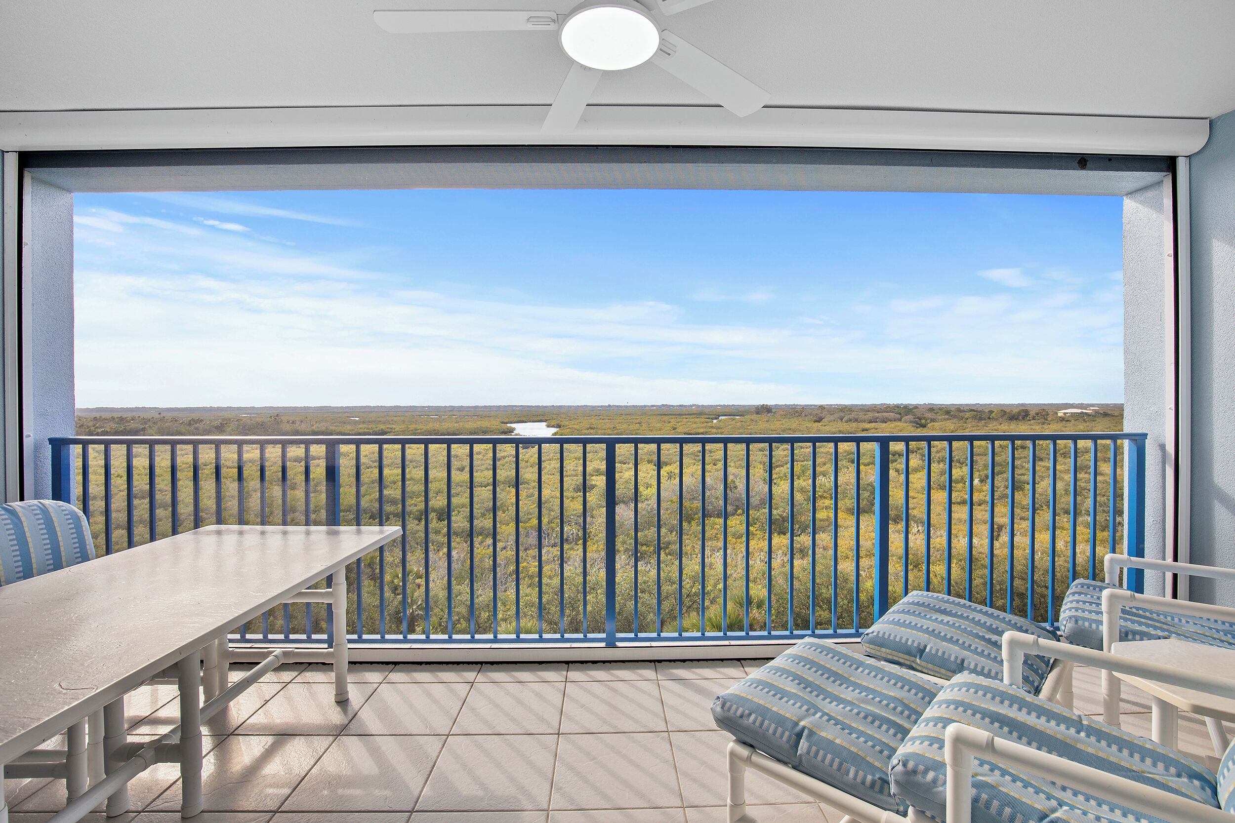 A balcony with a table and chairs, offering a view of a grassy landscape.