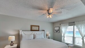 A bedroom with a bed, a nightstand, a ceiling fan, a window with curtains, and a framed picture on the wall. - Sea Oats #603 | Gulf Front Condo w/ Pool + Gym and Near Dining + Activities (Fort Walton Beach)