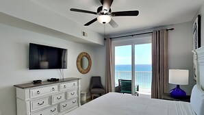 Une chambre d’hôtel équipée d’un lit, d’une télévision, d’un ventilateur de plafond, d’une commode, d’une chaise, d’une lampe et offrant une vue sur l’océan.