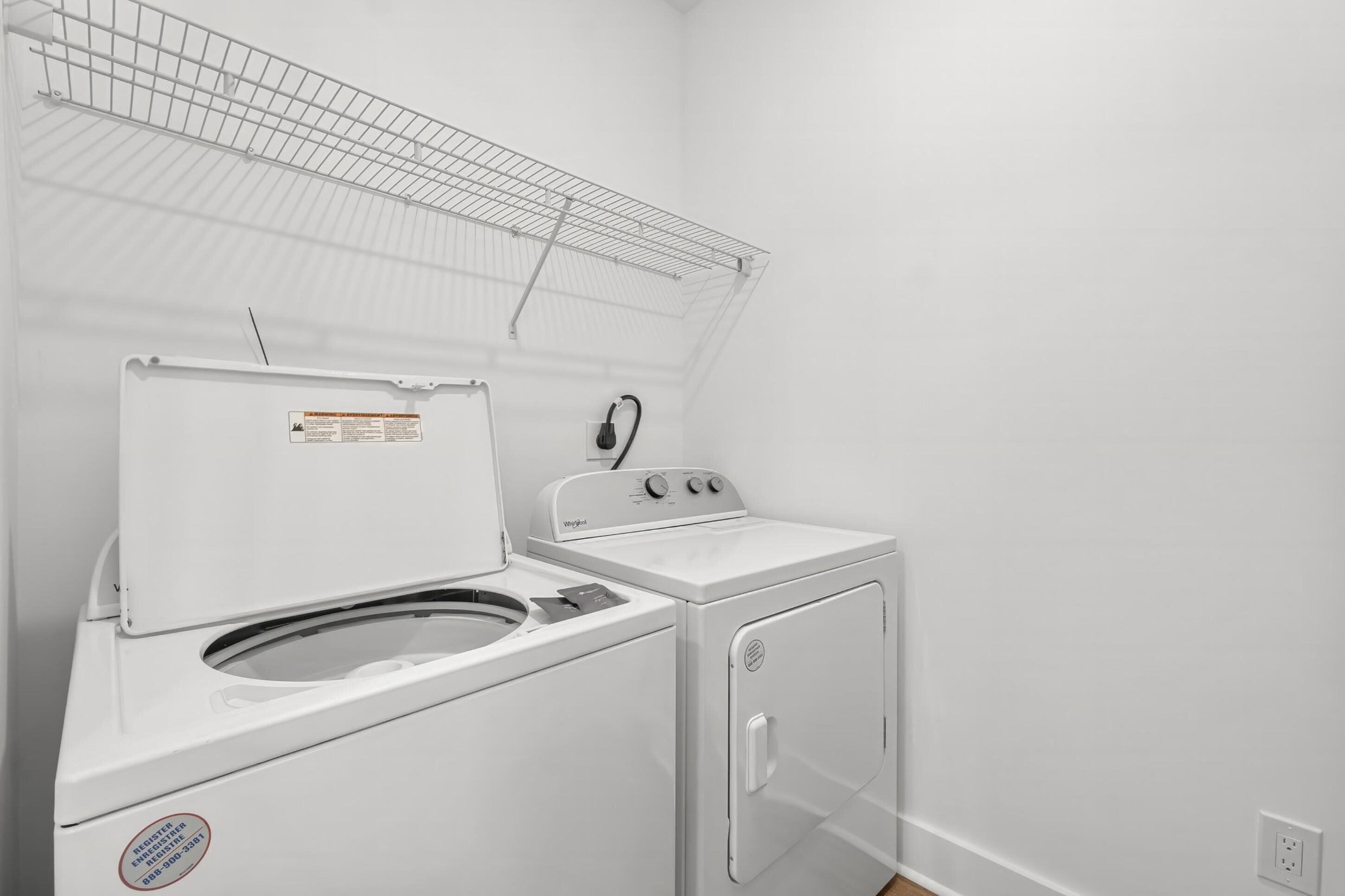 A laundry area with a front-loading washer and dryer, a metal drying rack, and a white wall.