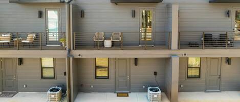 Un edificio residencial moderno de varios pisos con balcones, mobiliario exterior y un césped bien cuidado.
