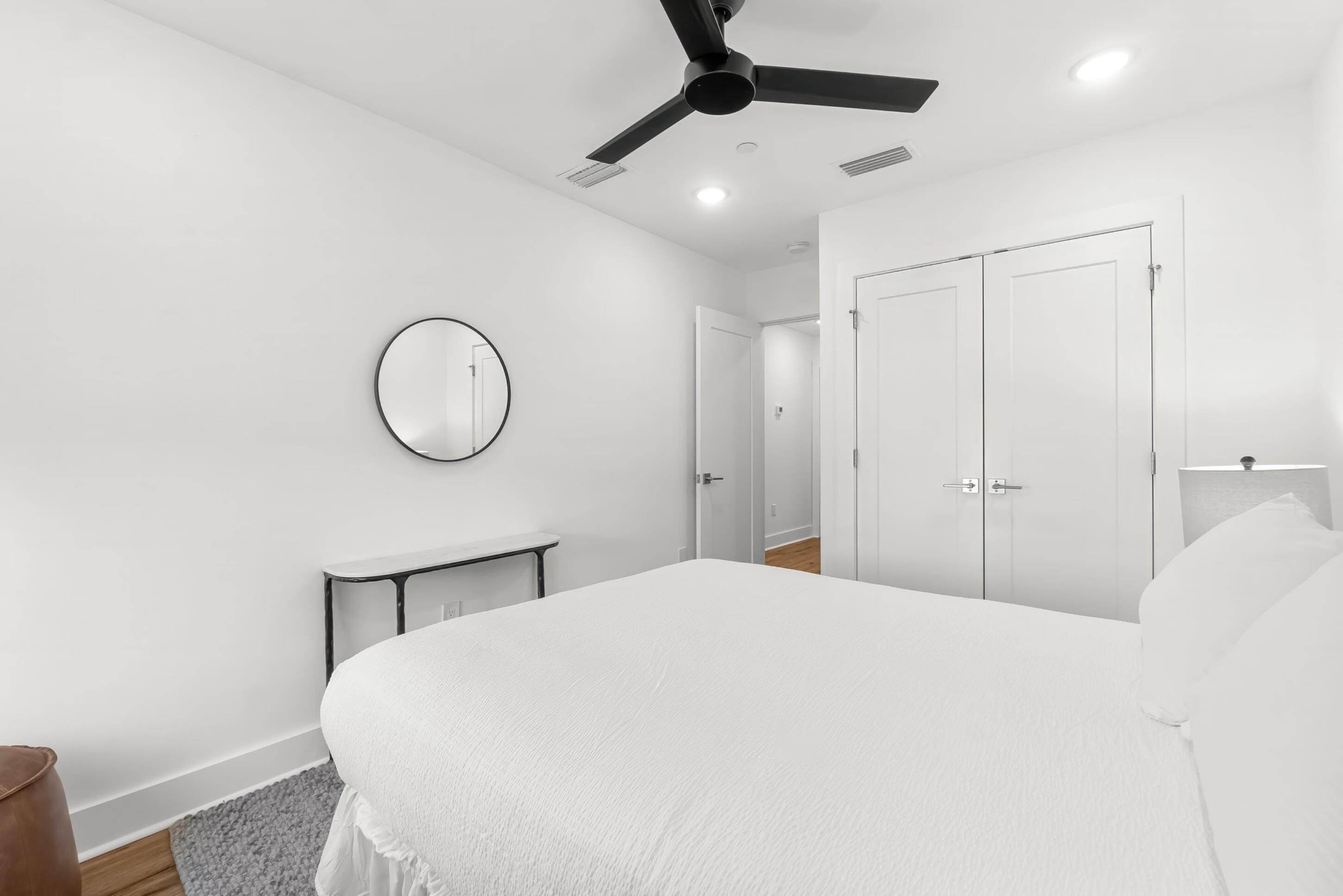 A bedroom with a bed, a ceiling fan, a round mirror, and white wardrobes.