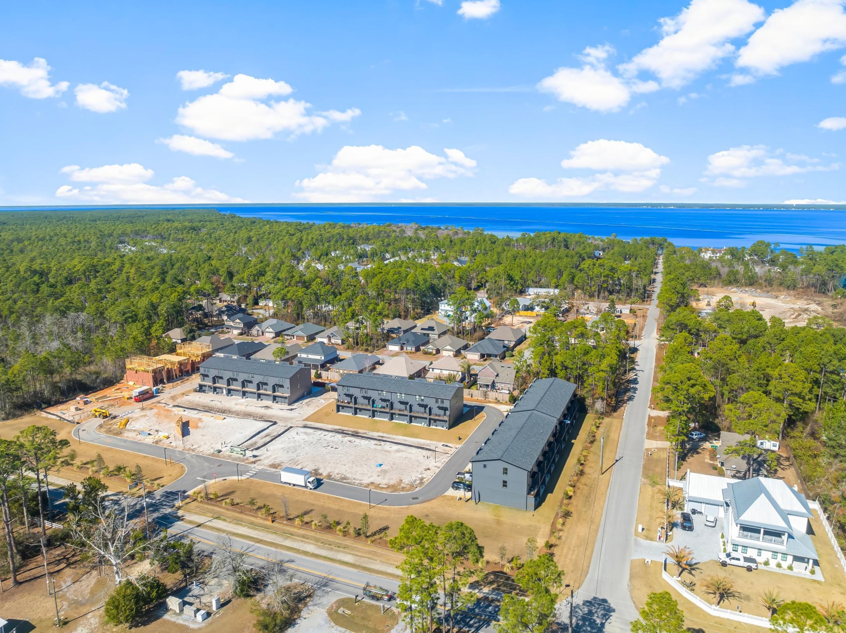 Une vue aérienne d’un quartier résidentiel avec de nombreuses maisons, un grand bâtiment en construction et une route menant à un plan d’eau.