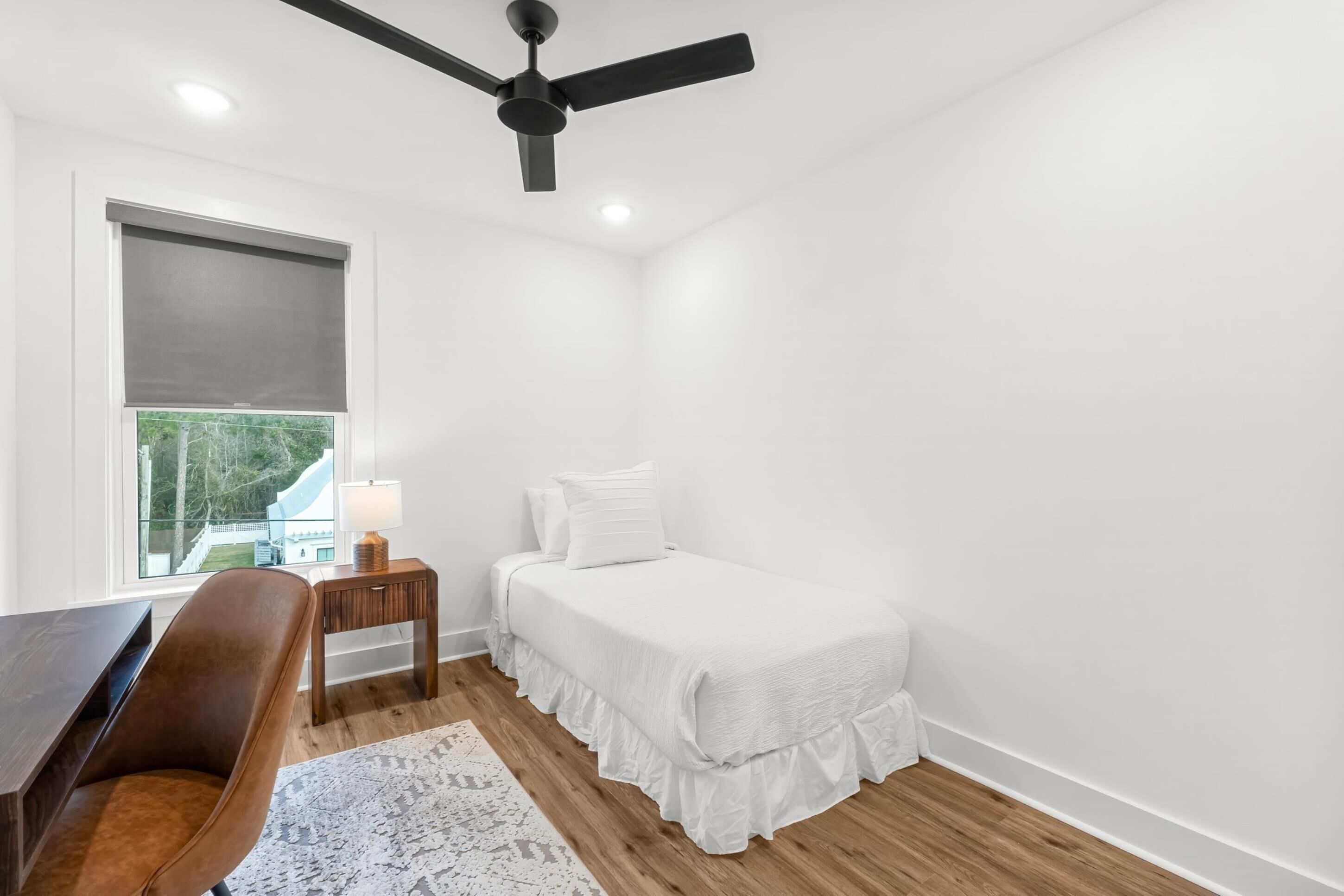 A bedroom with a bed, a desk, a chair, a nightstand, a lamp, and a ceiling fan.