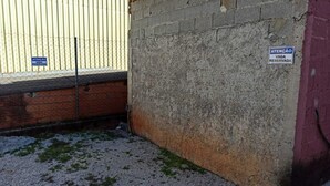 A corner of a building with a concrete wall and a metal fence. There are two signs: one on the fence and one on the wall. - Apartment 4 Great Location in Alumínio (Alumínio)