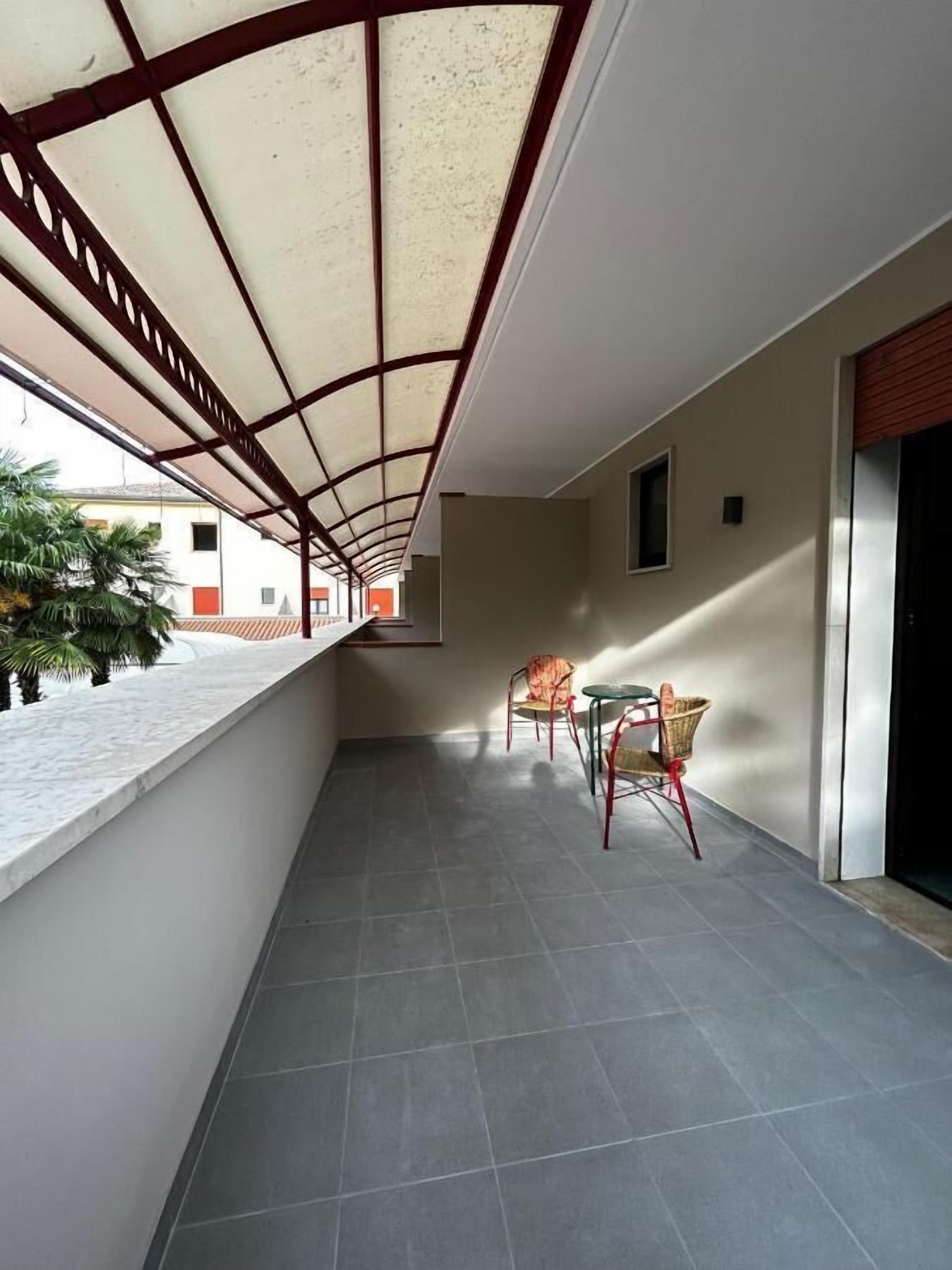 Un balcon couvert avec un sol carrelé, une table et des chaises, et une vue sur un bâtiment en arrière-plan.