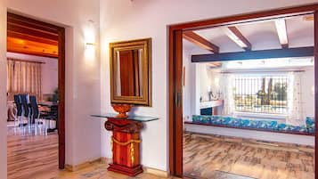 Une pièce avec un plafond en bois, une table en verre avec un pied rouge, un miroir encadré et une vue sur un espace extérieur comprenant une piscine et un banc.
