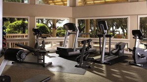 A gym with various exercise equipment, large windows, and a view of greenery outside.
