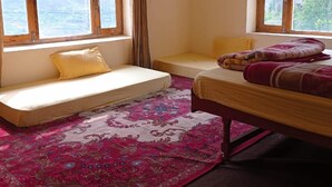 A room with two beds, a window with curtains, a hanging light fixture, and a patterned rug. - Lammaney Homestay (Lahul)