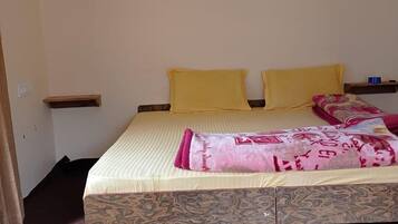A bedroom with a bed, two pillows, a patterned bedspread, a red carpet, and framed pictures on the wall.