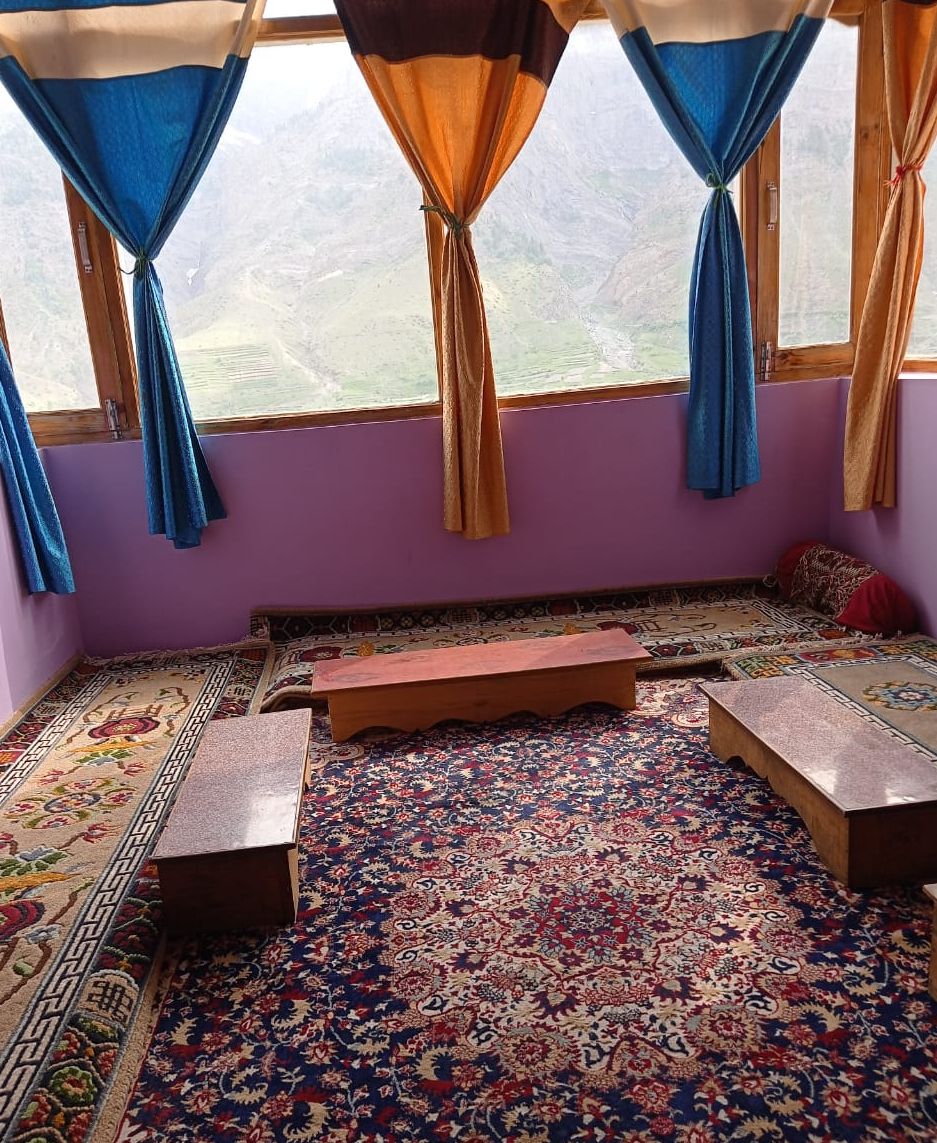 A room with a large window, a patterned carpet, and a wooden bench.