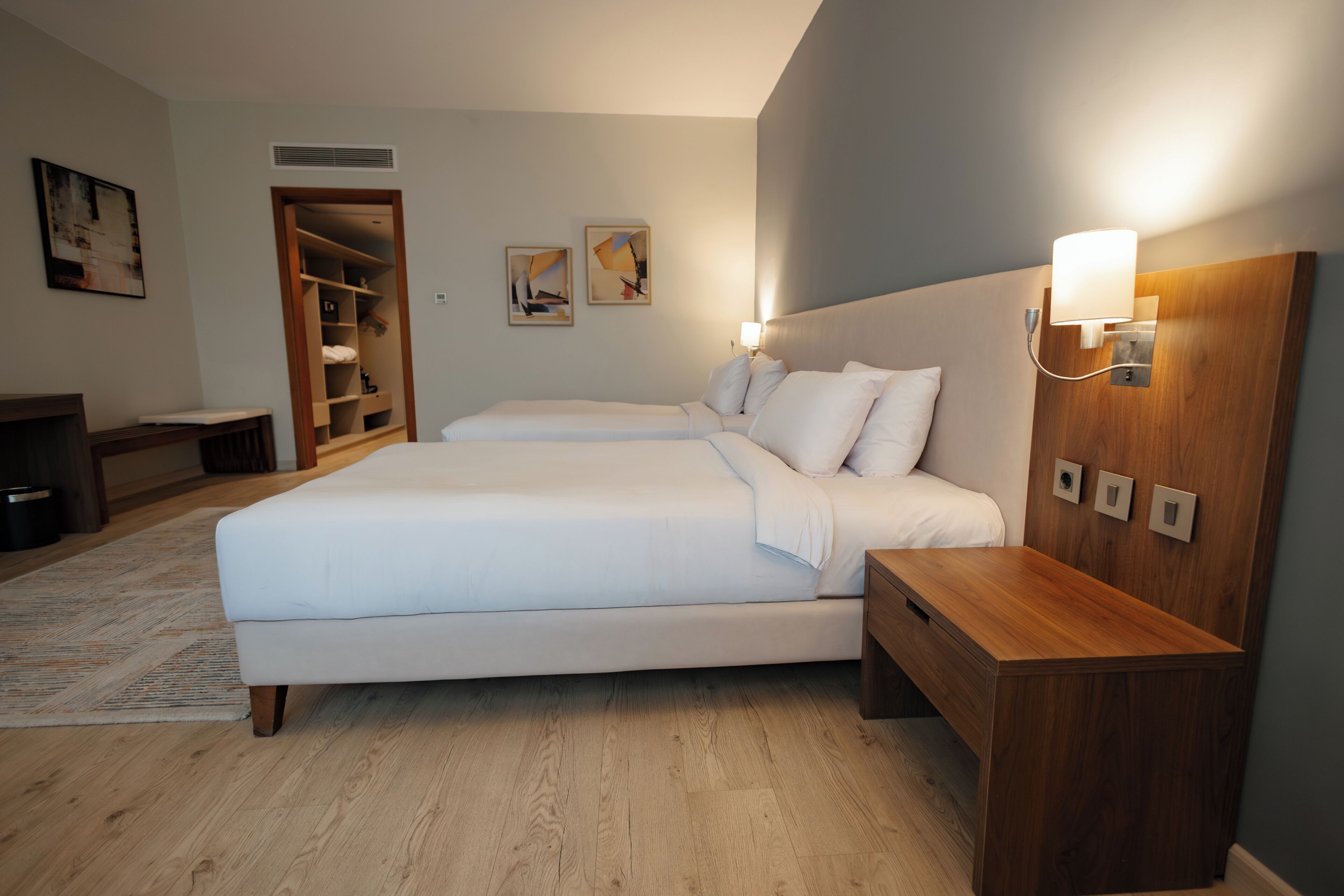 A hotel room with a double bed, a wooden nightstand, a bedside table, a wardrobe, and two wall-mounted light fixtures.