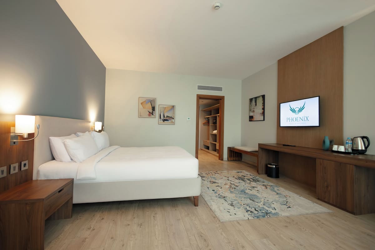 A modern hotel room with a bed, bedside tables, a TV, a desk, and a wardrobe.