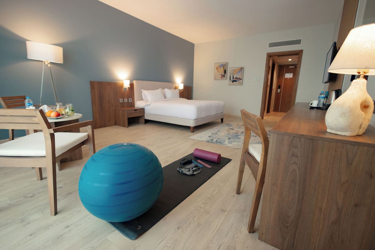 A hotel room with a bed, exercise ball, yoga mat, and a desk with a lamp.