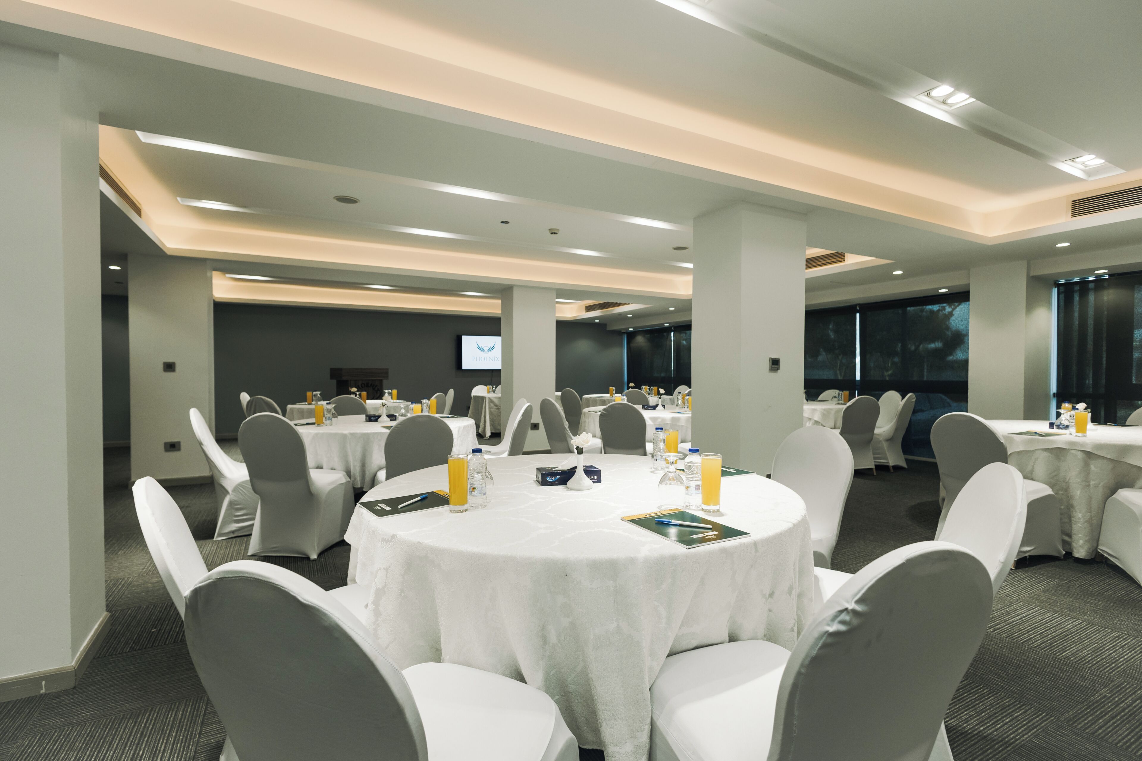 A conference room with round tables, white chairs, and a projection screen.