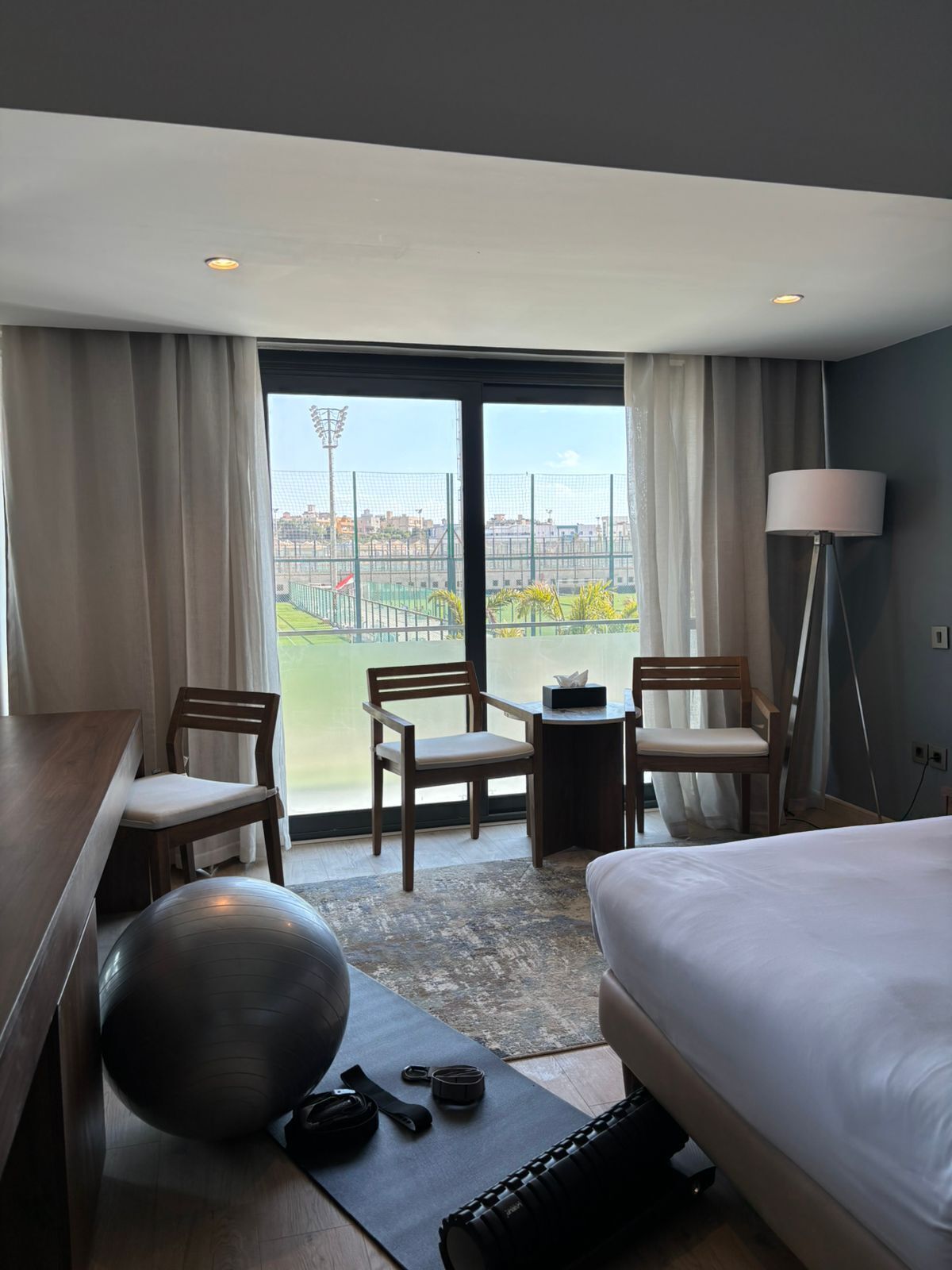 Une chambre d’hôtel équipée d’un lit, de deux chaises, d’un bureau, d’une lampe et de matériel d’exercice.