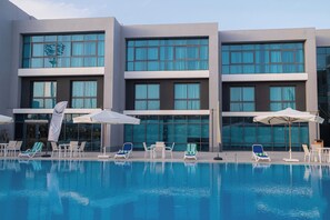 A modern hotel with a swimming pool, lounge chairs, and umbrellas. - Phoenix Hotel and Wellness (6th of October City)