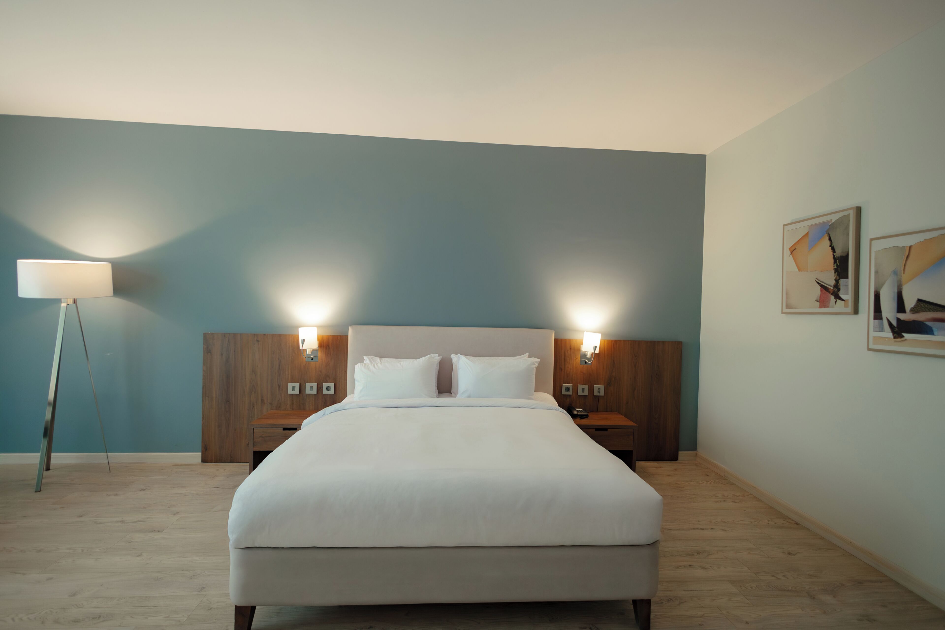 A hotel room with a large bed, bedside lamps, a nightstand, and a wall-mounted artwork.