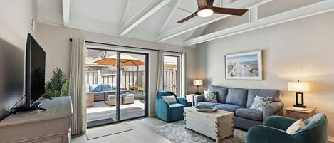 Un salón espacioso con ventilador de techo, televisor, sofá, mesa de centro y vistas a un patio exterior a través de puertas correderas de vidrio.