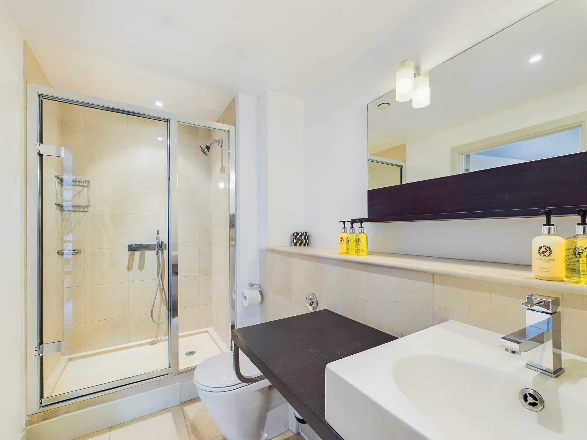 A modern bathroom with a glass shower enclosure, a white sink, and a dark countertop.