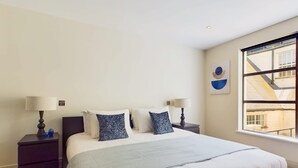 A bedroom with a large bed, two bedside tables, and a window with a view of a building. - Generous Covent Garden Apartment (London)