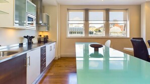 A modern kitchen with a glass dining table, stainless steel appliances, and large windows offering a city view. - Generous Covent Garden Apartment (London)