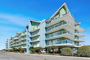 A multi-story hotel with balconies, a parking area, and a clear blue sky.