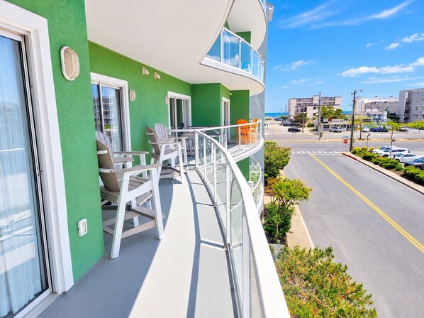 Un balcón con mobiliario exterior, vista despejada a la calle y un edificio con fachada verde.