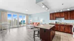 A spacious living area with a large window, a kitchen with wooden cabinets, and a dining area with a white table and chairs. - Gulf View Laketown Wharf 1BR/2BA condo unit 1013 (Panama City Beach)