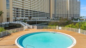 A pool area with a wooden deck, surrounded by a white railing. In the background, there are high-rise buildings with balconies. - Gulf View Laketown Wharf 1BR/2BA condo unit 1013 (Panama City Beach)