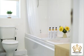 A bathroom with a toilet, a bathtub, and a shower area. There are toiletries on the edge of the bathtub.