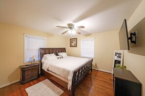 Un dormitorio con cama, mesita de noche, cómoda, ventilador de techo y televisor montado en la pared.