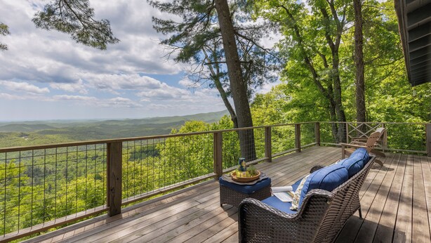 Eine Holzterrasse mit Korbmöbeln und Blick auf eine bewaldete Landschaft.