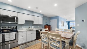 A modern kitchen with white cabinets, stainless steel appliances, and a dining area with wooden chairs and a table. - Midtown , 3 bedroom, 3 bathroom, 2 level condo, close to the beach (Ocean City)