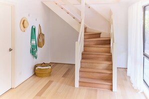 Staircase leads to an upper level, with woven baskets and a hat on the wall.