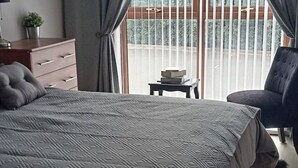 A bedroom with a patterned bedspread, a dresser, a chair, and a small table with books. - Sea Surf, 2 bedroom, fully equipped ground floor apartment, sleeps 4, in city (Bangor)