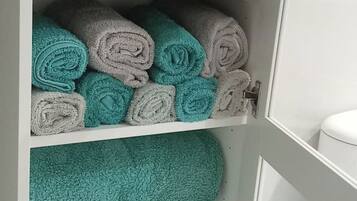 Een opbergkast met netjes opgerolde handdoeken in teal- en grijstinten.