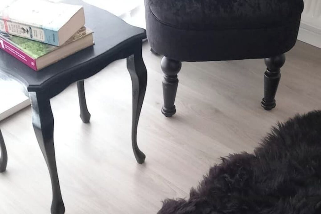 A room with a black armchair, a small wooden table with books, and a light-colored floor.