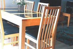 Un comedor con una mesa de vidrio, sillas de madera con cojines negros y un florero con flores sobre la mesa.