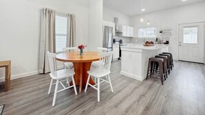 Una cocina moderna con armarios blancos, una isla central y un comedor con mesa de madera y sillas blancas.