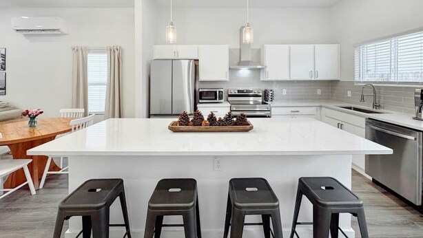 Una cocina moderna con una isla central, electrodomésticos de acero inoxidable e iluminación colgante.