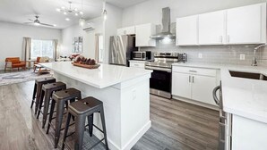 Una cocina moderna con armarios blancos, electrodomésticos de acero inoxidable y una isla central con taburetes de bar.
