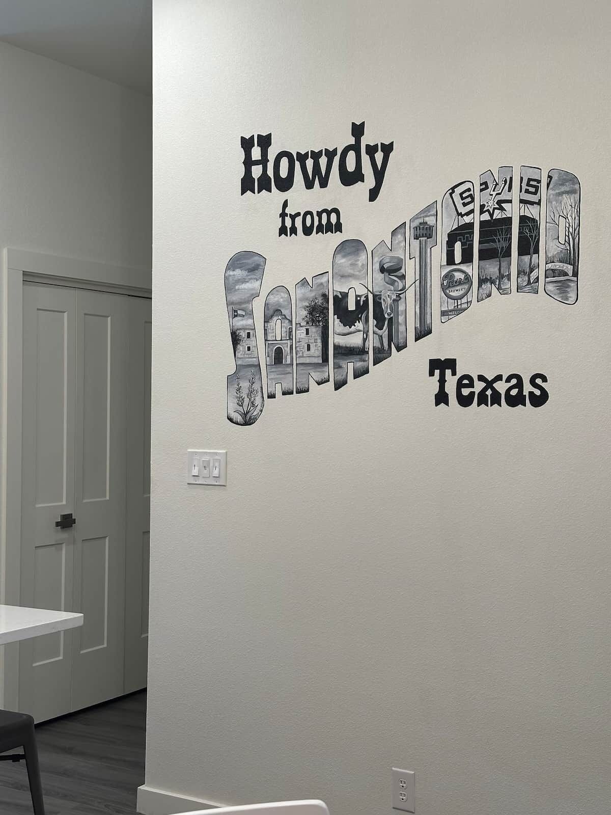 A wall with a Howdy from Texas mural, a white door, and a white electrical outlet.