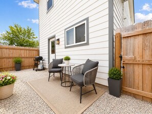 Eine Terrasse mit zwei Stühlen, einem Tisch, einem Grill und Kübelpflanzen.