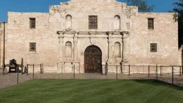 Un edificio histórico de piedra con un arco central en la puerta, flanqueado por columnas, y un techo plano con una pequeña torre.